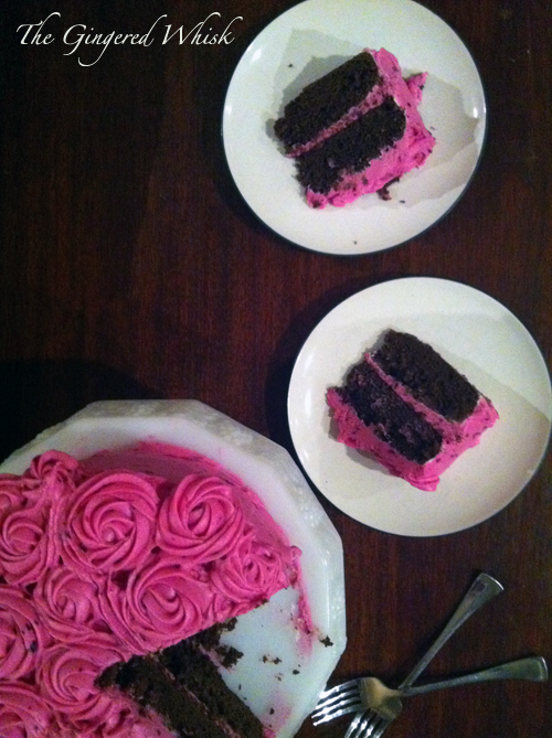 تصویری عمودی از بالا به پایین از یک کیک شکلاتی با رنگ صورتی و دو برش که روی صفحات سفید روی یک سطح چوبی قرار گرفته است.