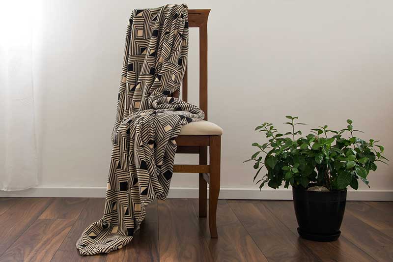 تصویر افقی نزدیک از گاردنیا گلدانی که روی یک کف چوبی در کنار یک صندلی قرار دارد.